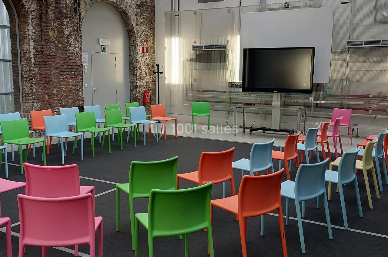 Salle de réunion moderne avec des chaises colorées disposées en cercle devant un écran noir.