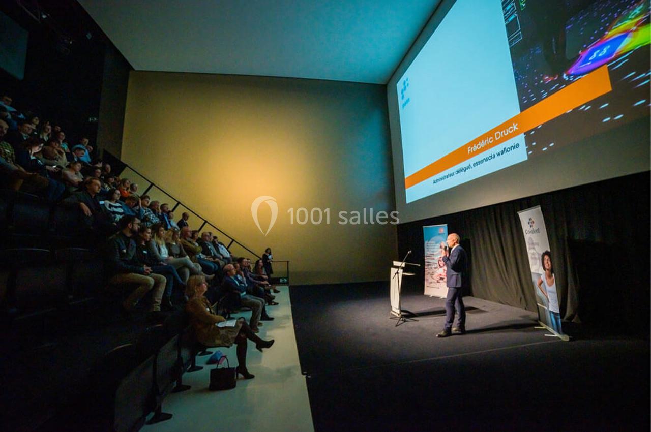 Un conférencier s'adresse à un public assis dans une salle sombre avec une grande projection à l'écran.