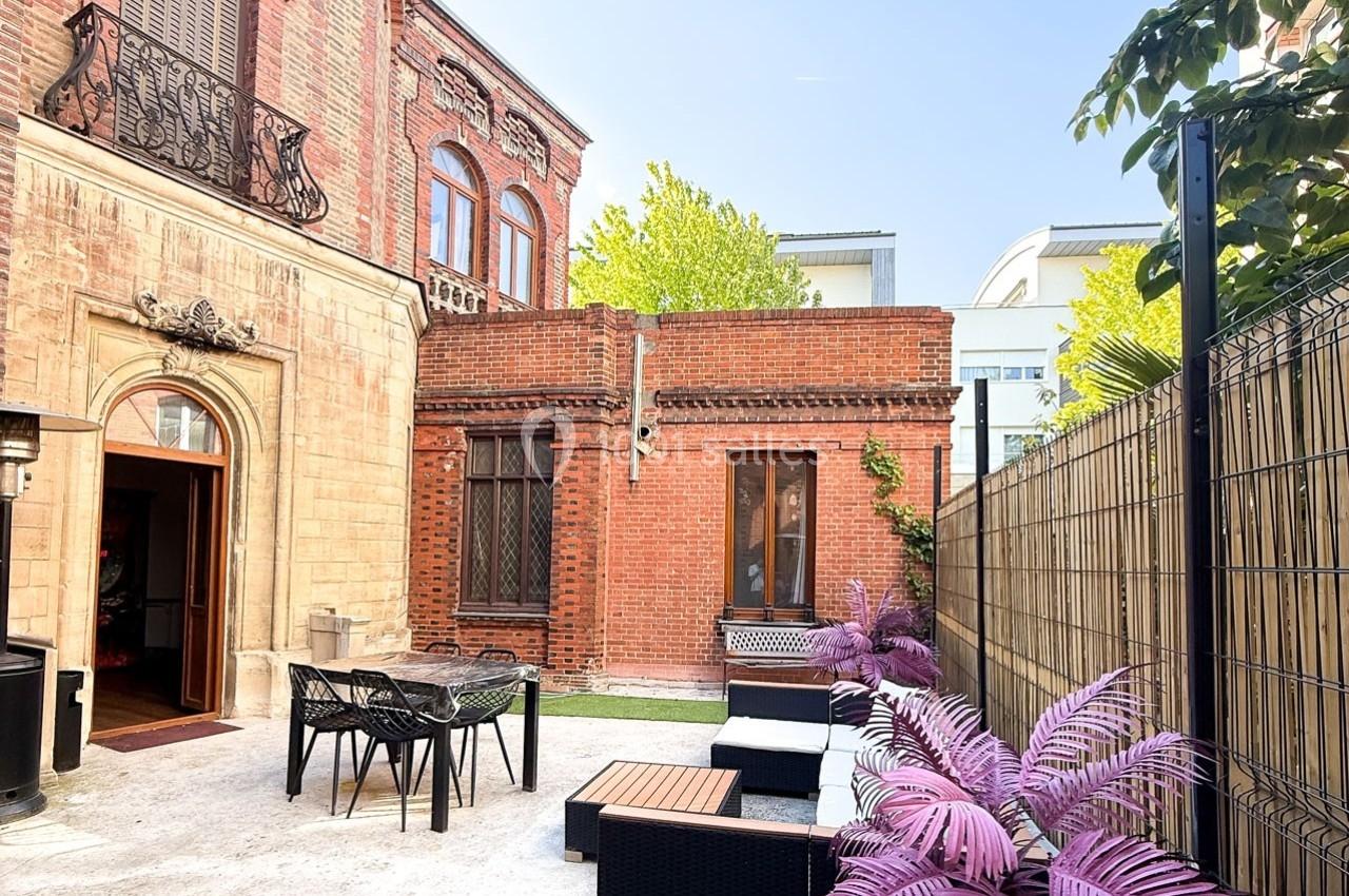 Cour extérieure avec mobilier de jardin, murs en briques rouges, plantes décoratives et clôture en bambou.