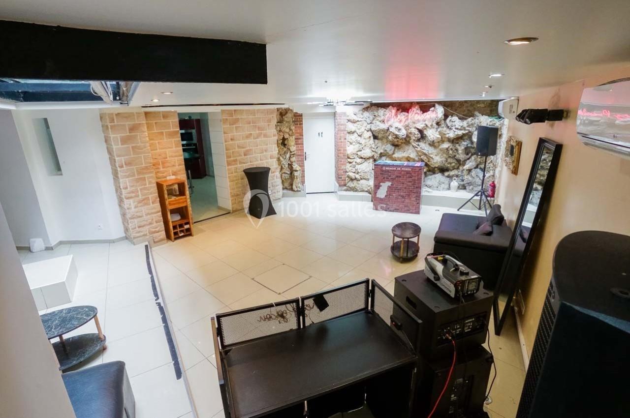 Salle lumineuse avec murs en pierre apparente, mobilier minimaliste et espace équipé pour des événements ou soirées.