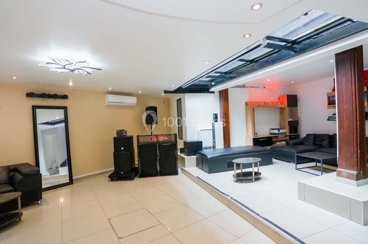 Salle moderne avec canapés, tables basses, miroirs, système audio et éclairage, sol en carrelage clair.