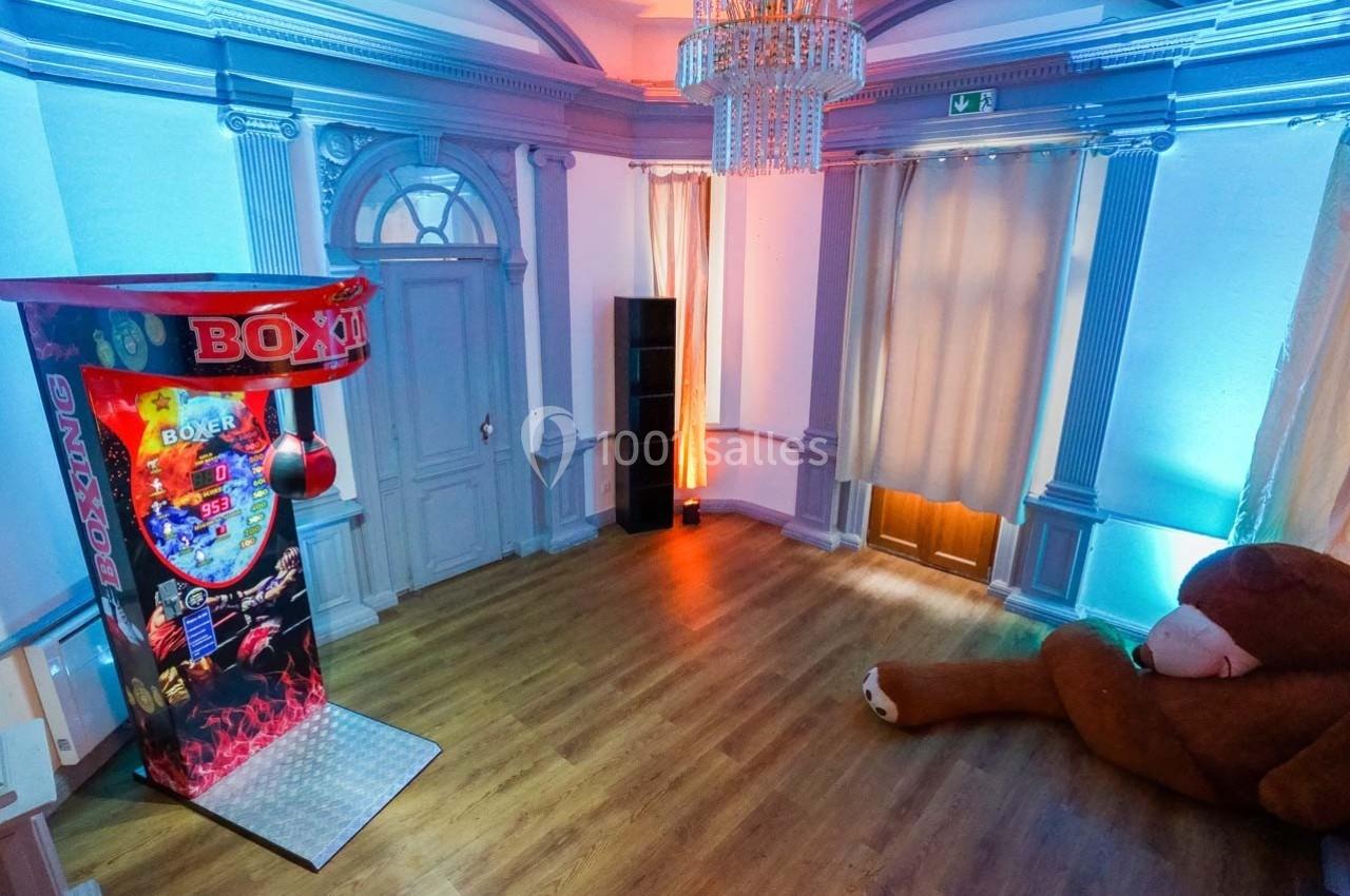 Salle avec un jeu de boxe lumineux, un grand ours en peluche au sol et un éclairage coloré.