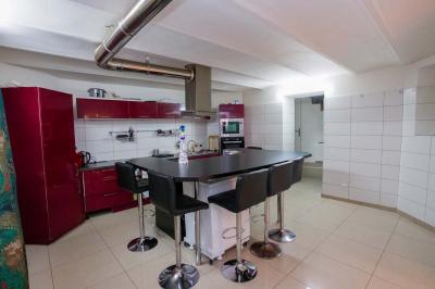 Cuisine moderne avec îlot central noir, chaises hautes, meubles rouges, électroménagers intégrés et carrelage blanc.