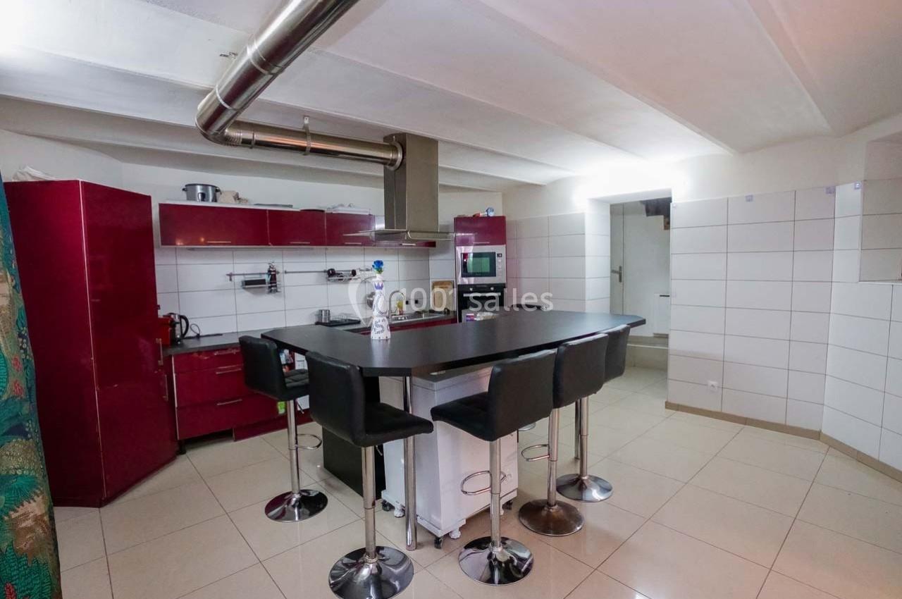 Cuisine moderne avec meubles rouges, îlot central noir, tabourets hauts et carrelage clair au sol et aux murs.