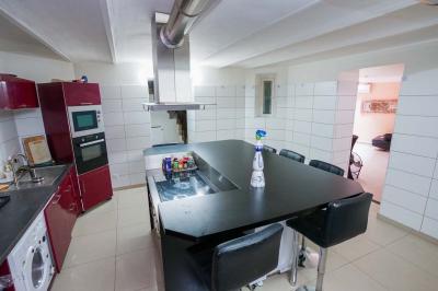 Cuisine moderne avec îlot central noir, chaises hautes, meubles rouges, électroménagers intégrés et carrelage blanc.