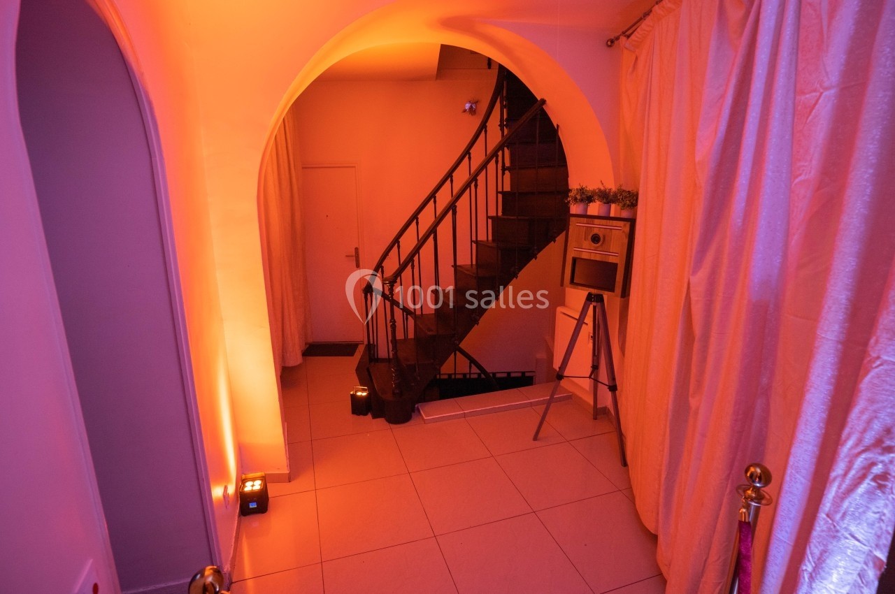 Escalier en colimaçon noir dans un intérieur éclairé par une lumière orange, avec rideaux et décor minimaliste.