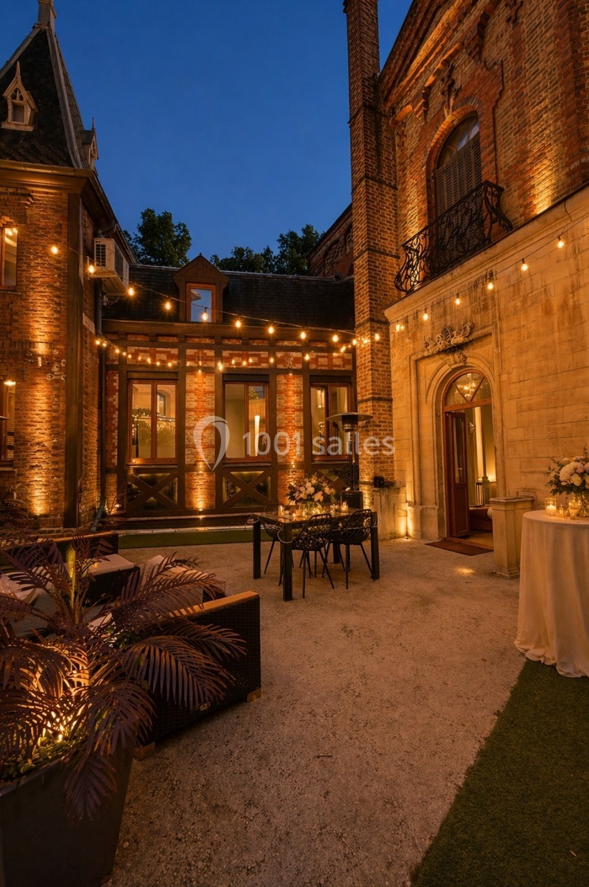 Location salle Nanterre (Hauts-de-Seine) - Manoir Loft 92 #7 Cour extérieure d'un bâtiment en briques éclairée par des guirlandes lumineuses, avec tables décorées pour un événement.