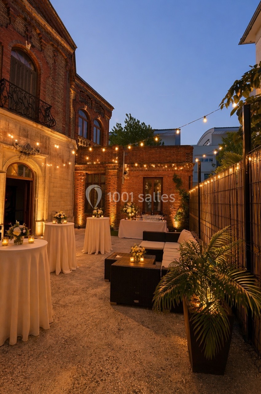 Location salle Nanterre (Hauts-de-Seine) - Manoir Loft 92 #8 Cour extérieure éclairée par des guirlandes lumineuses, avec tables hautes décorées et mobilier de salon en soirée.