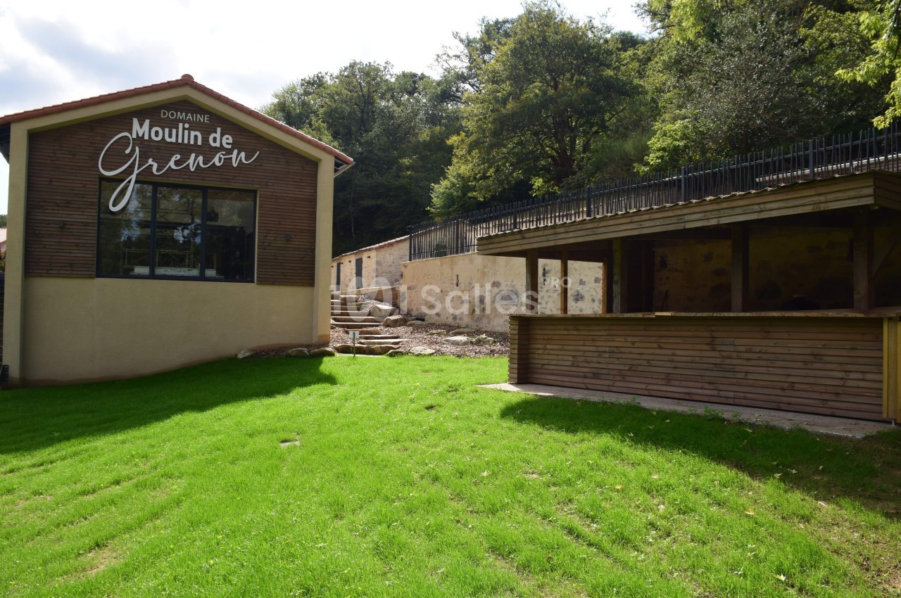 Bâtiment moderne avec une enseigne ’Domaine Moulin de Grenon’, terrasse en bois et espace vert environnant.