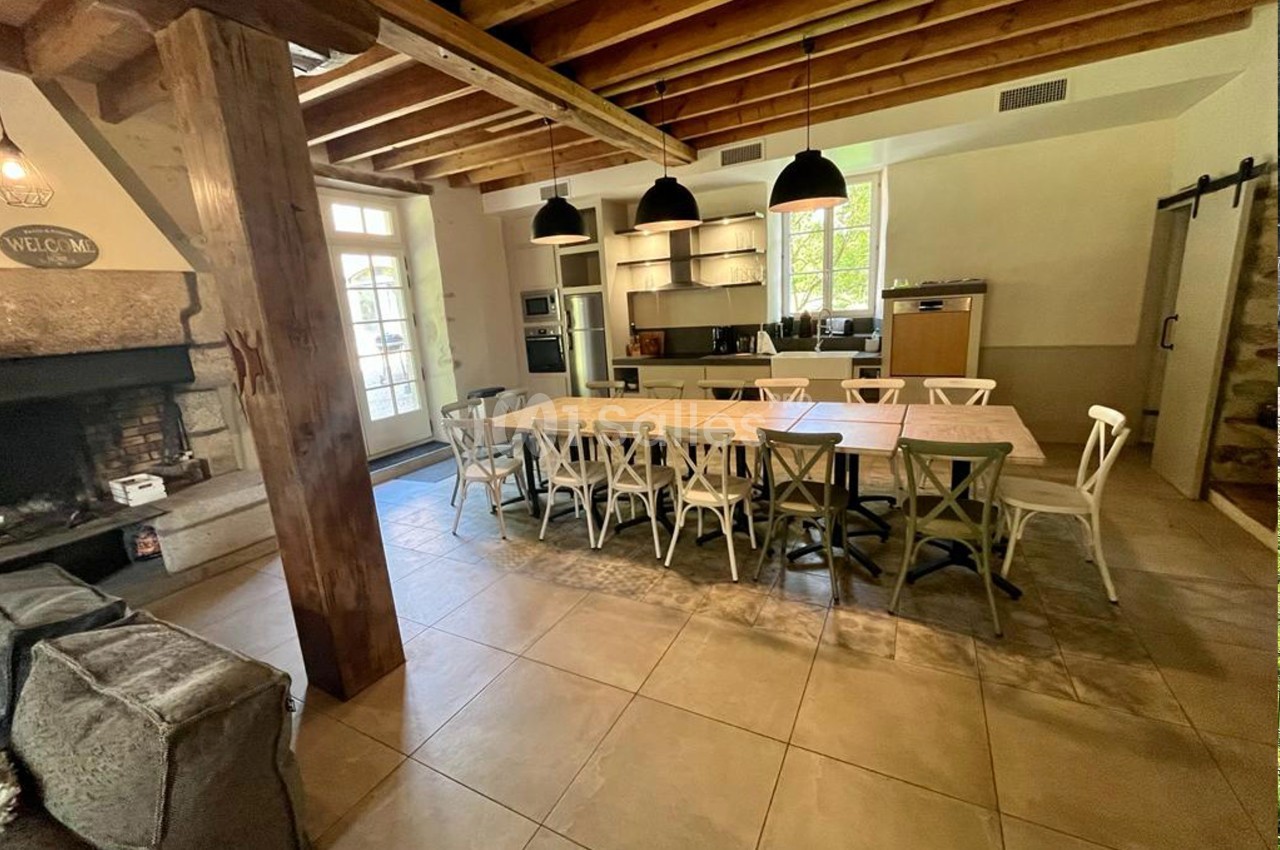 Salle à manger avec une grande table entourée de chaises, une cuisine ouverte et une cheminée en pierre.