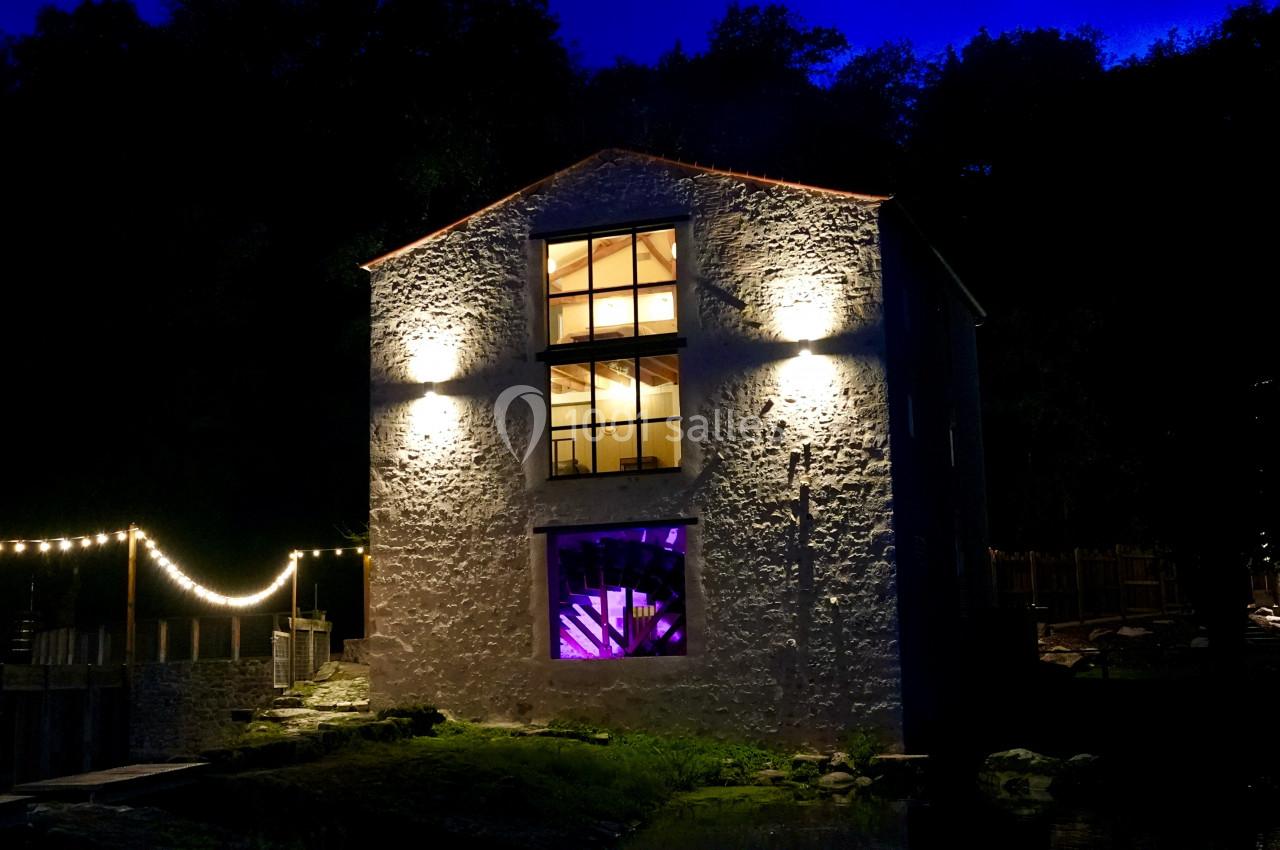 Façade d'un bâtiment en pierre éclairé la nuit, avec des lumières décoratives et une fenêtre illuminée en violet.