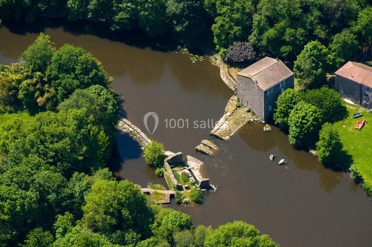Vue aérienne d'un ancien moulin en pierre bordant une rivière entourée de végétation dense.