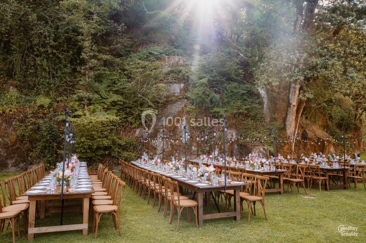 Tables dressées pour un repas en plein air dans un cadre naturel, entourées de végétation et éclairées par le soleil.