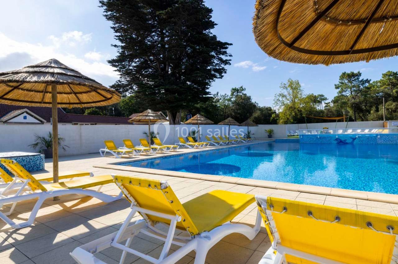 Chaises longues jaunes et parasols en paille disposés autour d'une piscine extérieure sous un ciel dégagé.