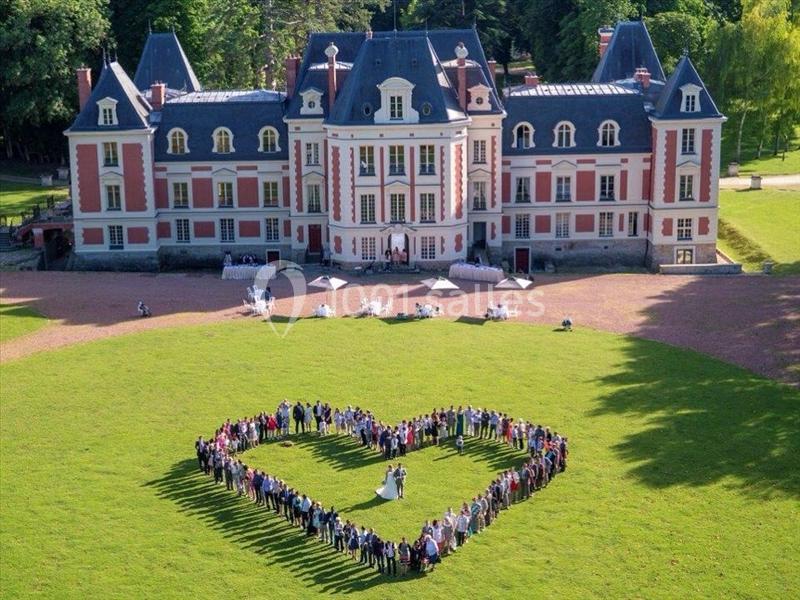 Un groupe de personnes formant un cœur autour d'un couple sur une pelouse devant un château.