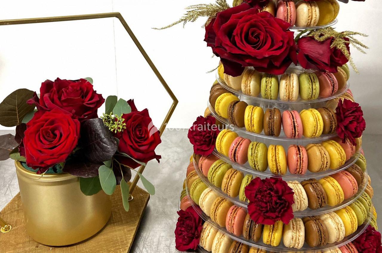 Tour de macarons colorés décorée de roses rouges, accompagnée d'un bouquet dans un vase doré.