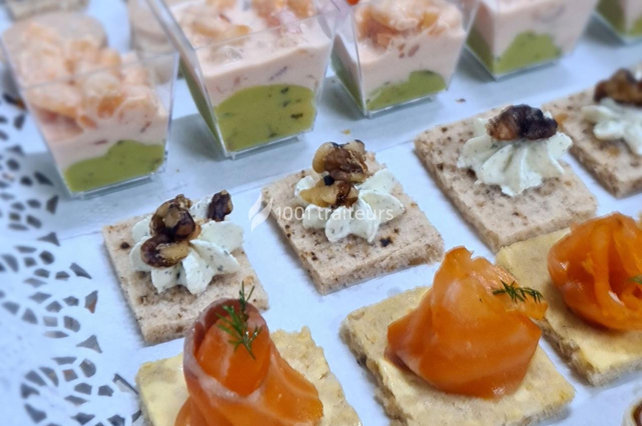 Assortiment de canapés avec saumon fumé, crème aux noix et verrines de crevettes sur une nappe blanche.