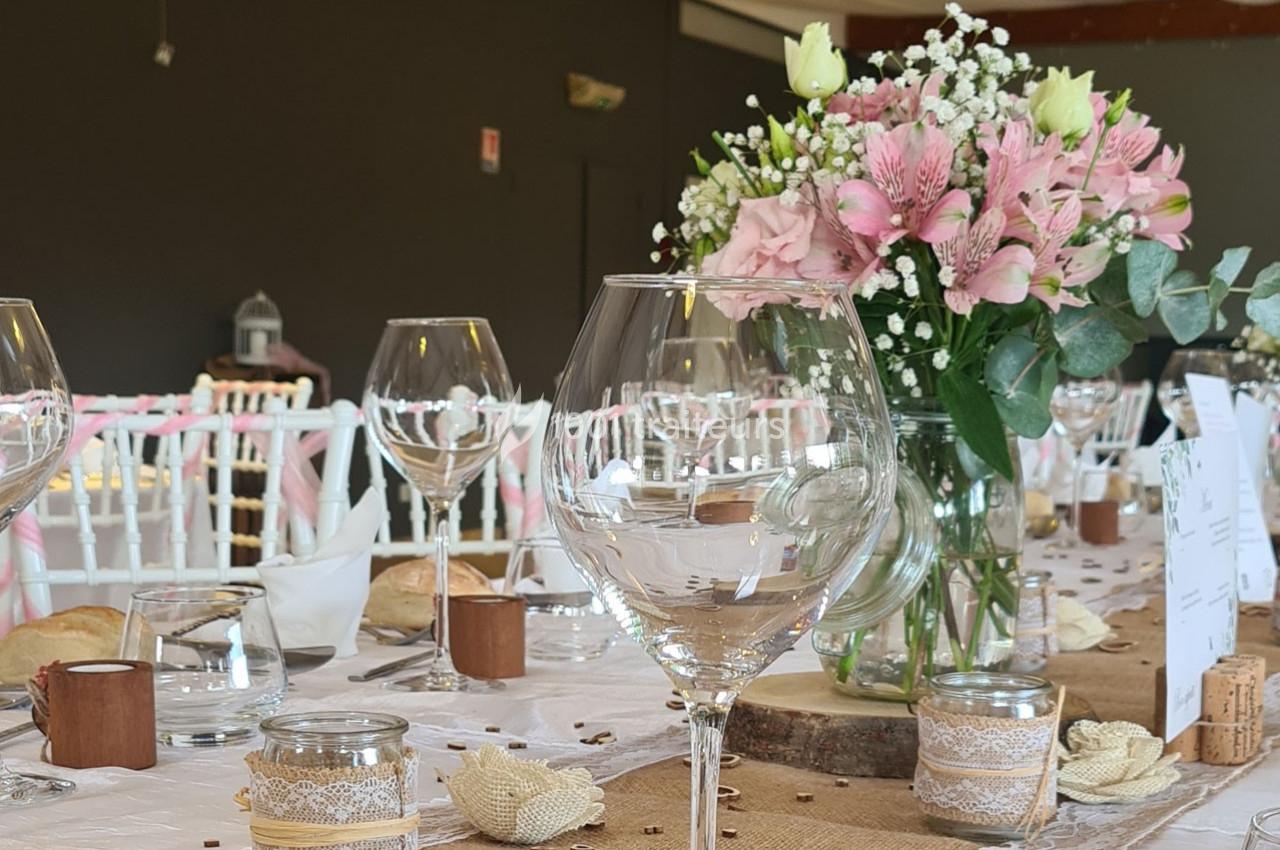 Table décorée pour un événement avec nappes en lin, fleurs roses et blanches, verres à vin et petits pots en verre.