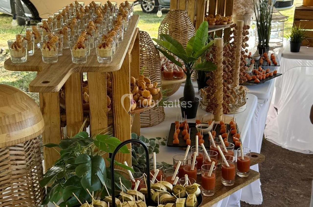 Buffet de réception en extérieur avec verrines, brochettes et autres amuse-bouches présentés sur des supports en bois.