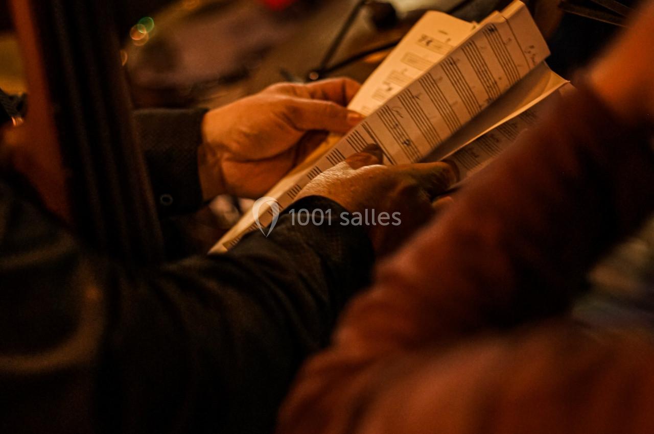 Des musiciens lisent une partition dans une ambiance tamisée, avec un saxophone visible en arrière-plan.