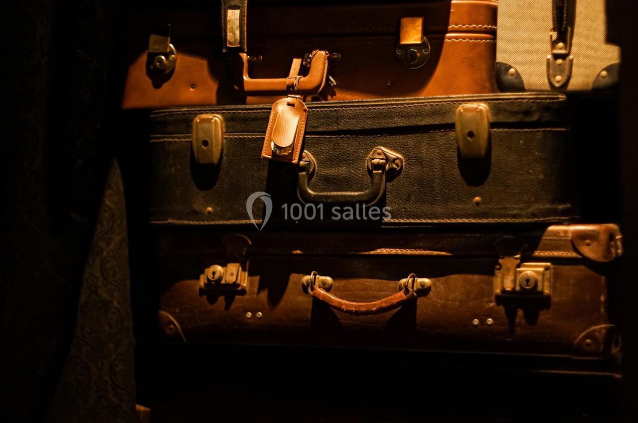 Pile de valises vintage en cuir et en tissu, de différentes tailles et couleurs, empilées dans un espace sombre.