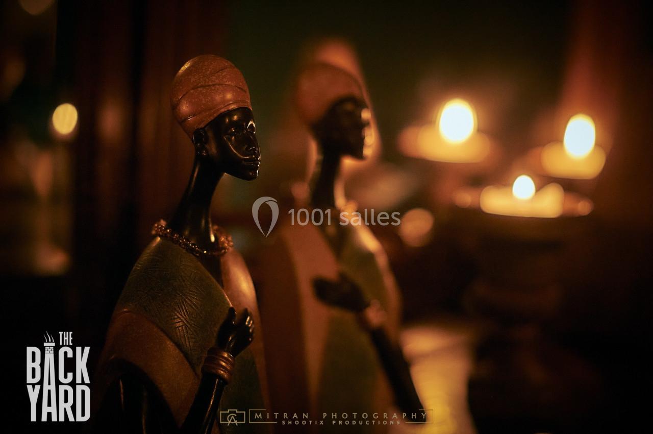 Deux statuettes africaines en gros plan, éclairées par des bougies en arrière-plan dans une ambiance tamisée.