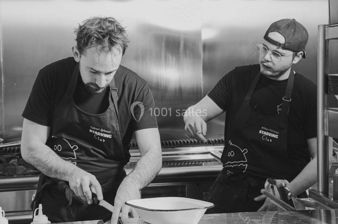 Deux cuisiniers en tablier préparent des ingrédients dans une cuisine professionnelle.