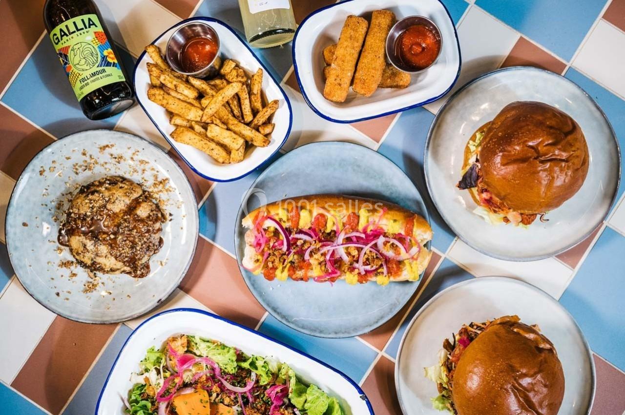 Assortiment de plats comprenant burgers, hot-dog, salade, frites, mozzarella sticks, bière et bouteille de vin.