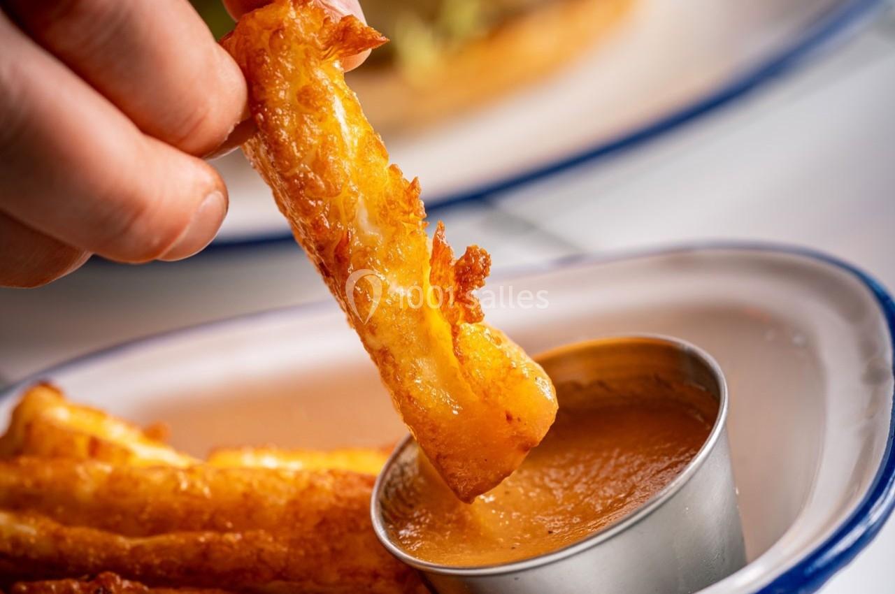 Frites croustillantes trempées dans une sauce dorée, servies dans une assiette blanche avec bord bleu.