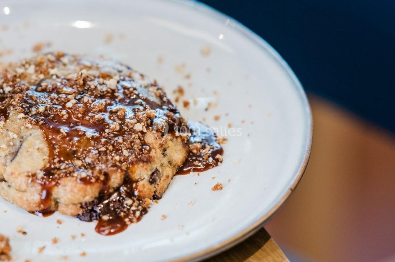 Cookie aux pépites de chocolat nappé de caramel et parsemé de miettes sur une assiette blanche.