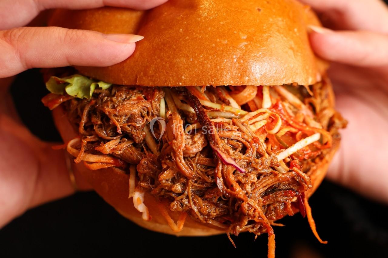 Burger garni de viande effilochée et de légumes croquants, tenu par deux mains.