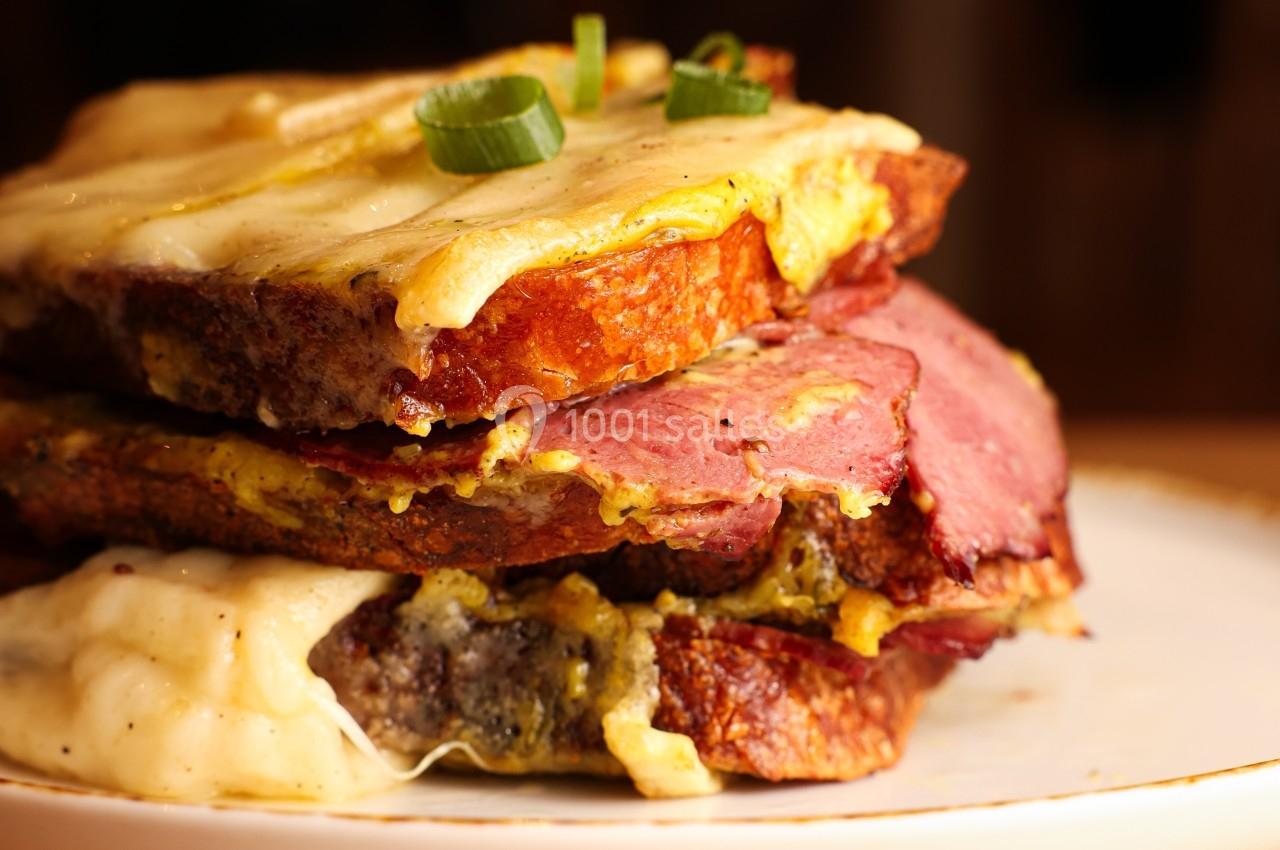 Sandwich garni de viande fumée, fromage fondu et pain grillé, décoré de rondelles d'oignon vert.