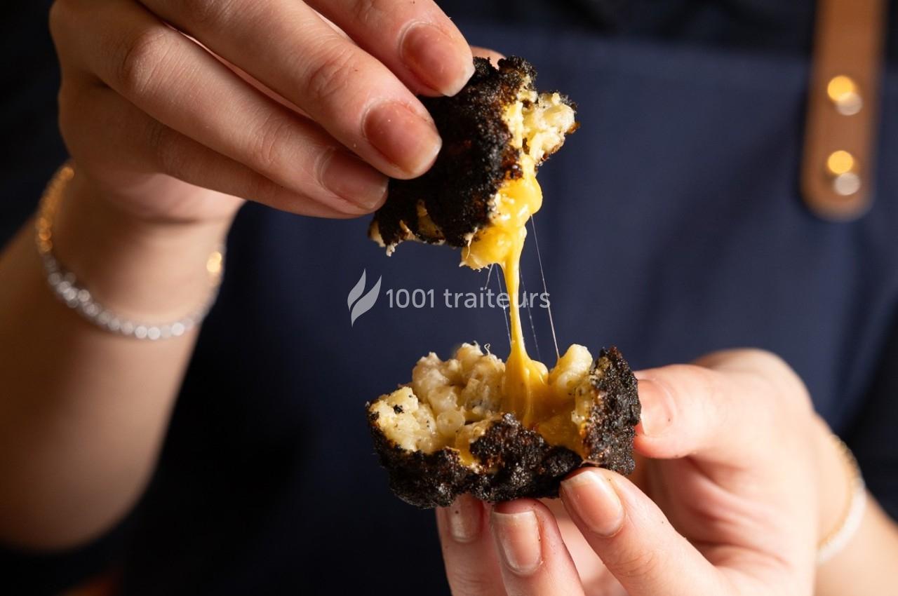 Une personne ouvre un beignet noirci, révélant un fromage fondu qui s'étire à l'intérieur.