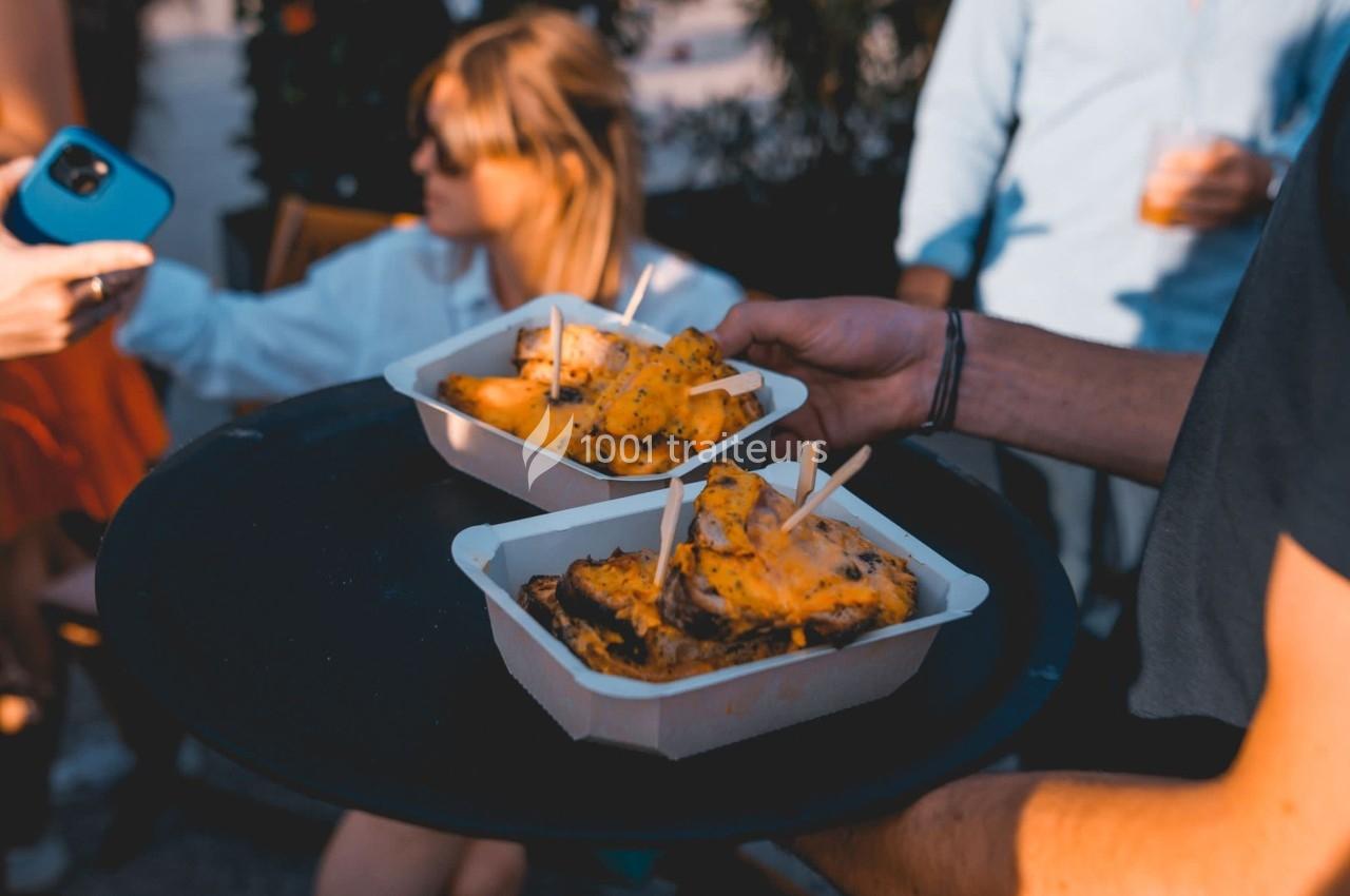 Deux barquettes de frites garnies de fromage servies sur un plateau lors d'un événement en extérieur.