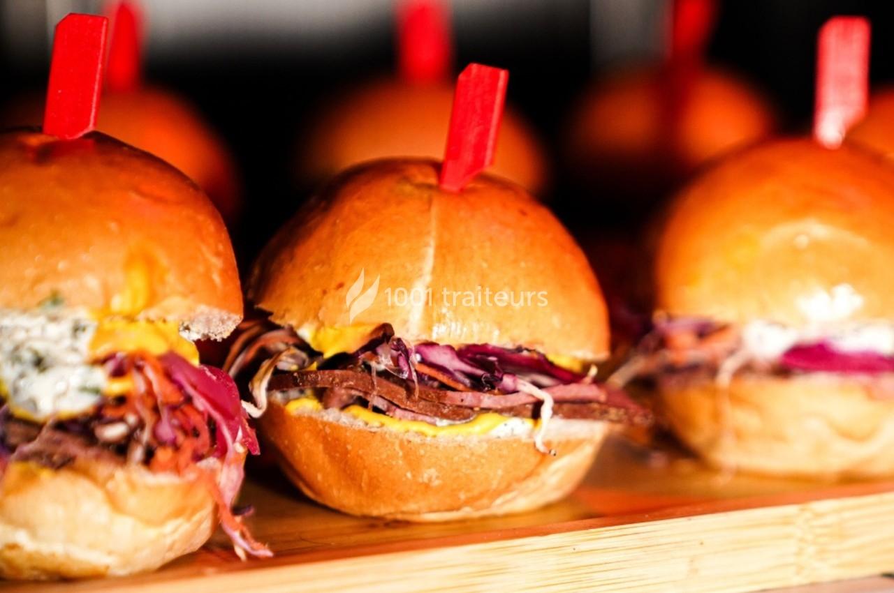 Petits burgers garnis de viande effilochée, coleslaw coloré et sauce, présentés sur une planche en bois.