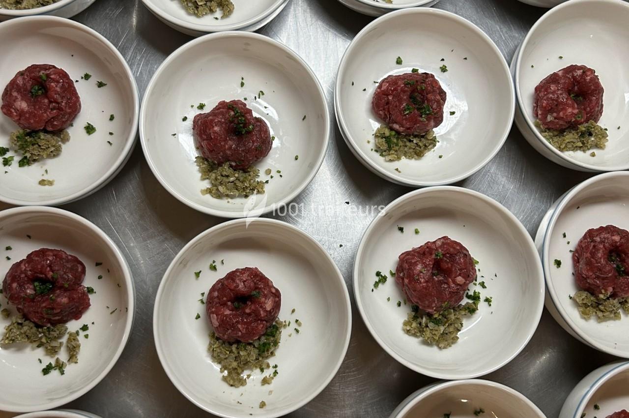 Assiettes individuelles contenant des portions de tartare de viande crue garnies d'herbes et accompagnées d'une préparation…