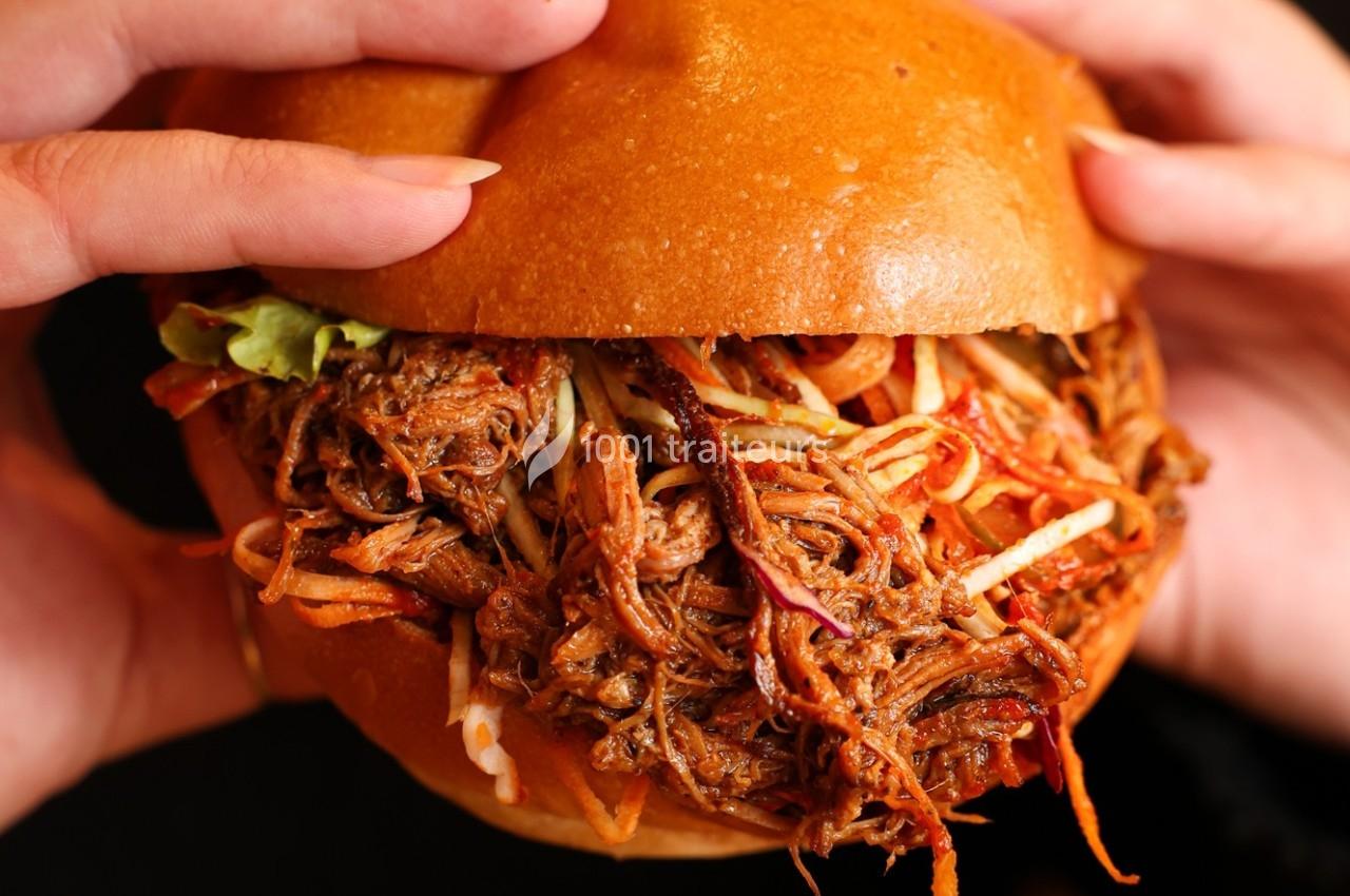 Burger garni de viande effilochée et de légumes croquants, tenu par deux mains.