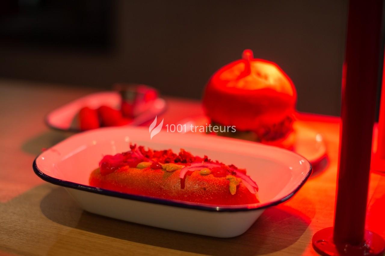 Plat de street food composé d'un hot-dog garni et d'un burger, éclairé par une lumière rouge sur une table en bois.
