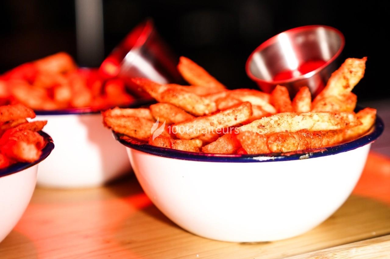 Bol de frites dorées assaisonnées, servi avec une petite coupelle en métal sur une table en bois.
