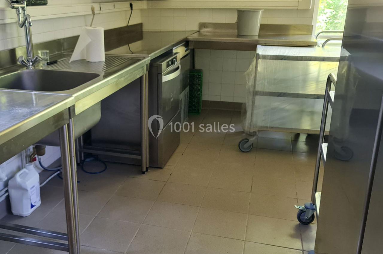 Cuisine professionnelle avec évier, lave-vaisselle, plan de travail en inox et chariot sur roulettes.