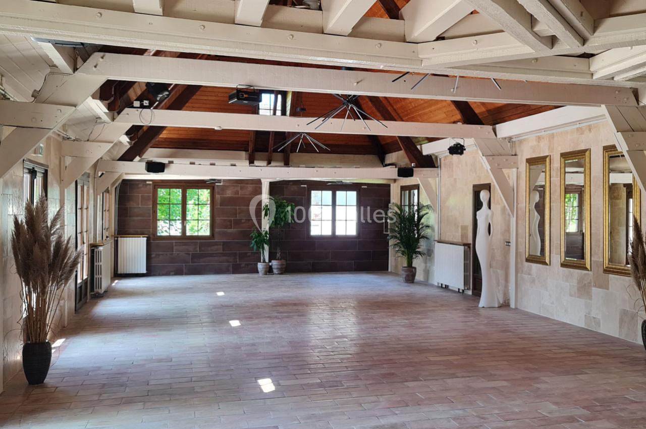 Salle spacieuse avec poutres apparentes, grandes fenêtres, murs en pierre et décorations végétales.
