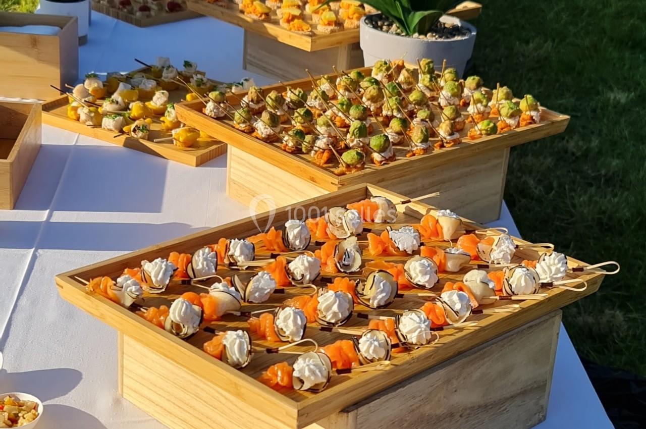 Buffet en plein air avec une variété de bouchées salées et sucrées présentées sur des plateaux en bois.