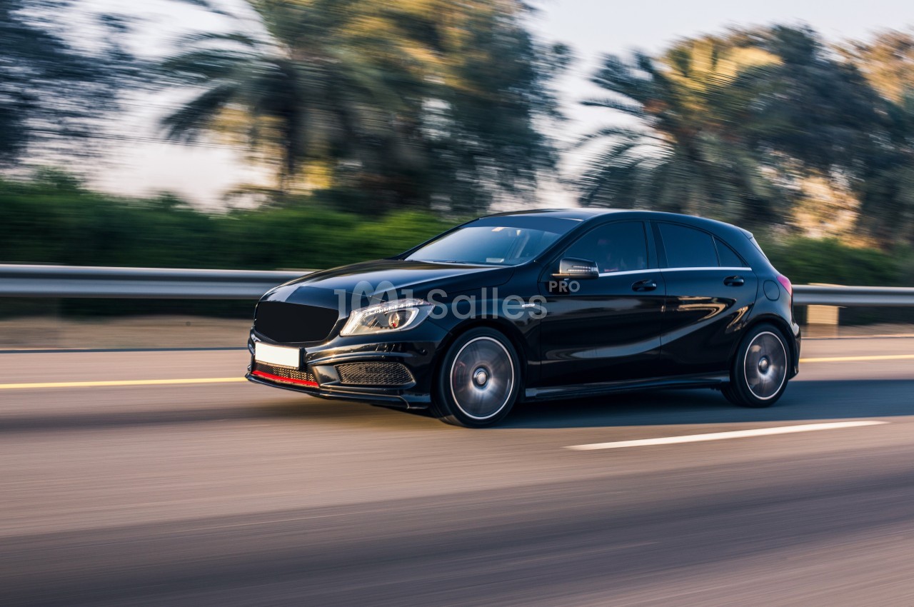 Voiture noire compacte roulant sur une route bordée de palmiers par temps clair.