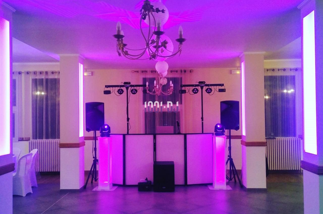 Salle de réception éclairée en rose avec une piste de danse, des enceintes et un équipement de DJ installé.