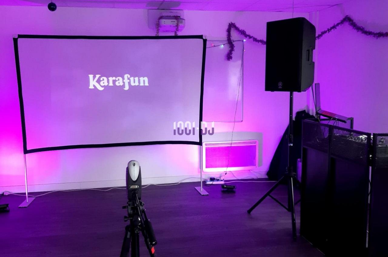 Écran de karaoké avec projecteur, haut-parleurs et décorations lumineuses dans une salle équipée.