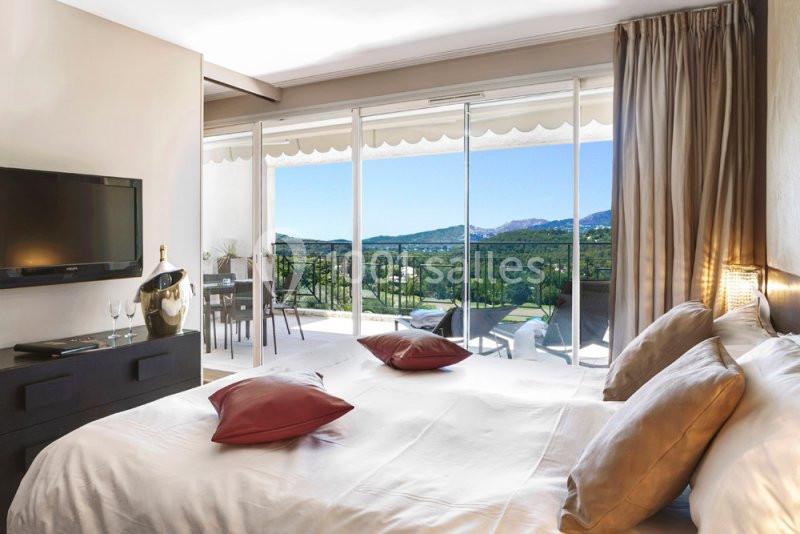 Chambre lumineuse avec lit double, télévision, terrasse aménagée et vue sur un paysage verdoyant et montagneux.