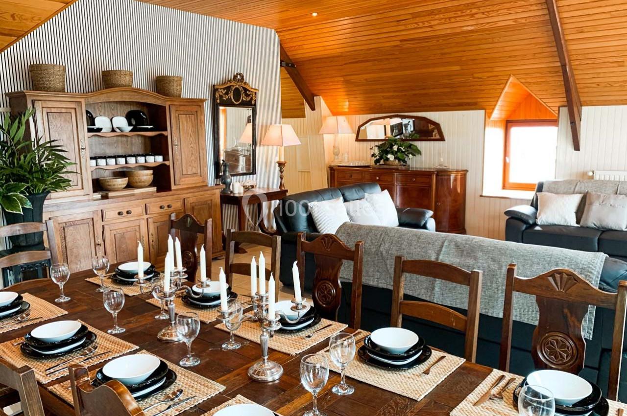 Salle à manger et salon avec mobilier en bois, table dressée, canapés, et décoration chaleureuse sous un plafond en bois.