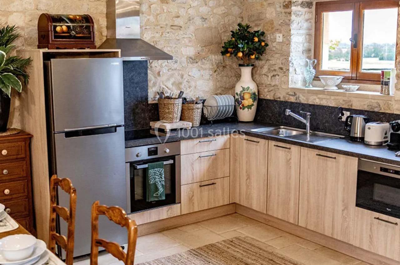 Cuisine rustique avec murs en pierre, meubles en bois clair, électroménagers modernes et fenêtre donnant sur l'extérieur.