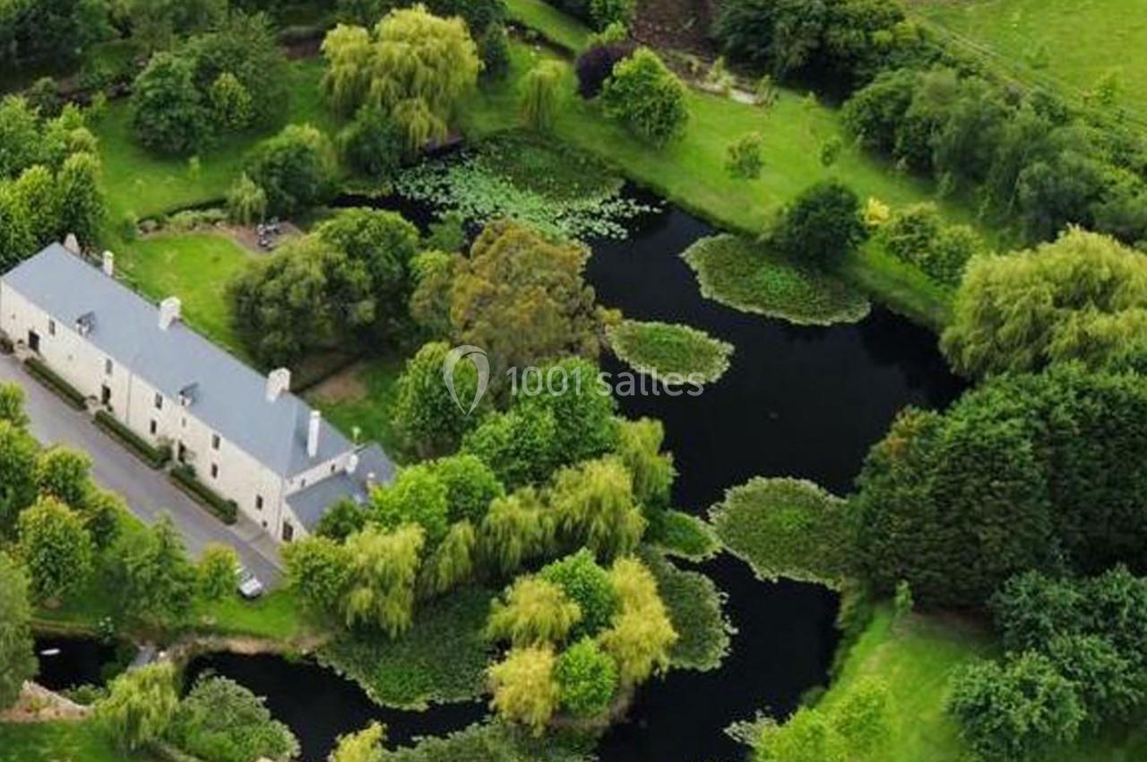 Vue aérienne d'un domaine avec un étang entouré de verdure, arbres et bâtiments résidentiels.