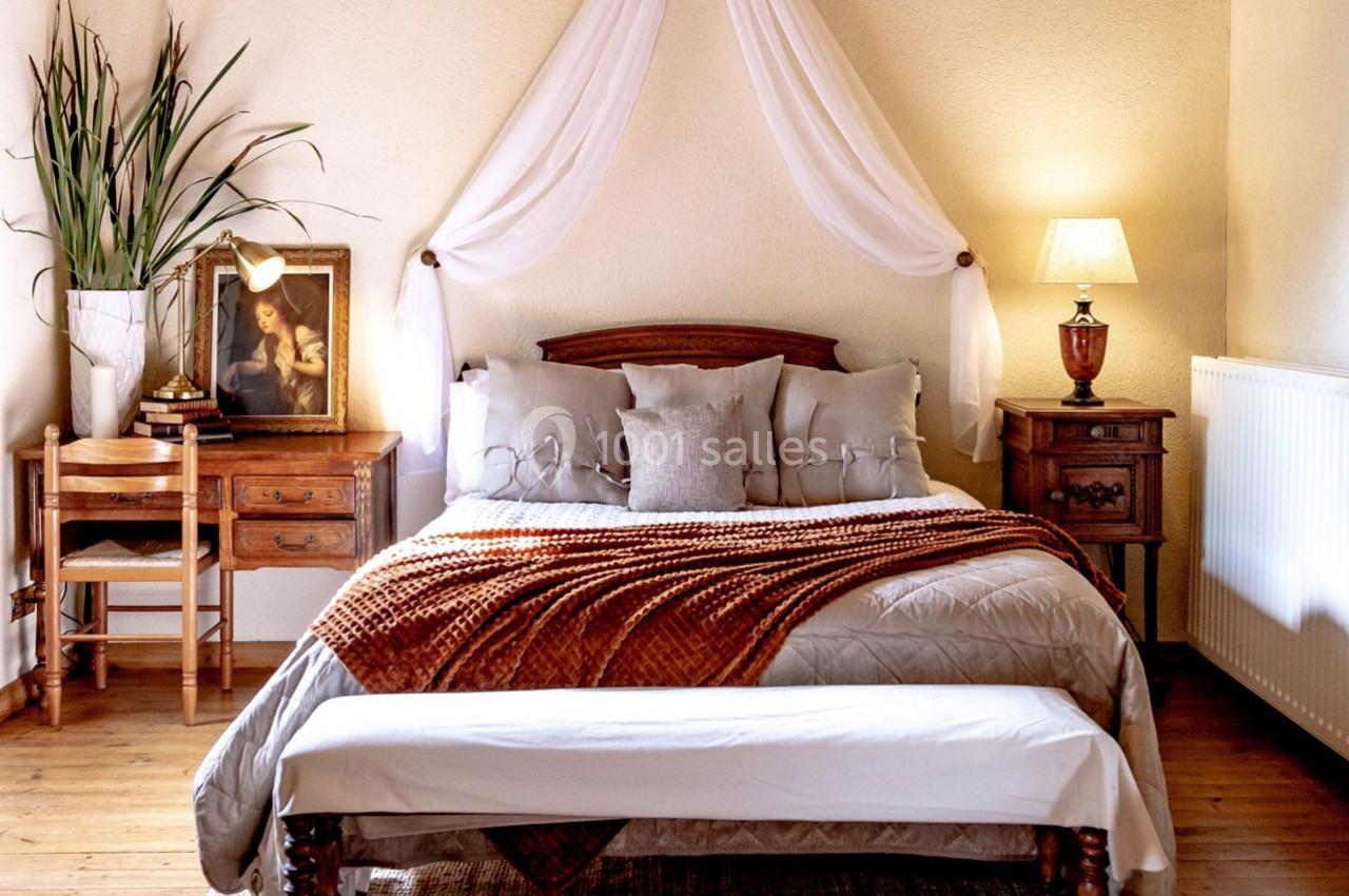 Chambre lumineuse avec lit double, plaid orange, tables de chevet, lampe, bureau en bois et décoration sobre.